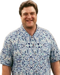 A smiling man wearing a short-sleeve button-up shirt with a blue, white, and light teal geometric pattern, set against a plain white background.