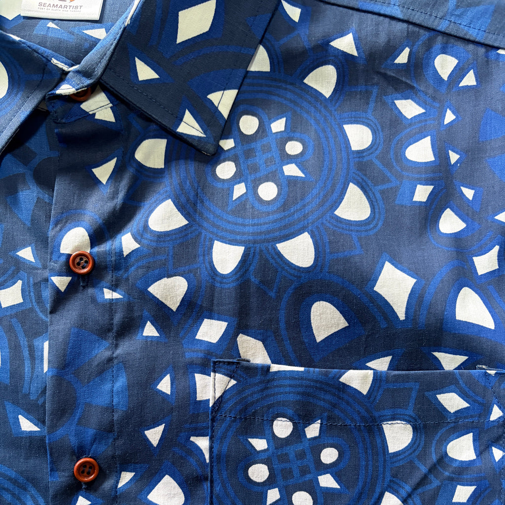 Close-up of a blue and white patterned button-down shirt with brown buttons, showing the collar, front placket, and chest pocket.