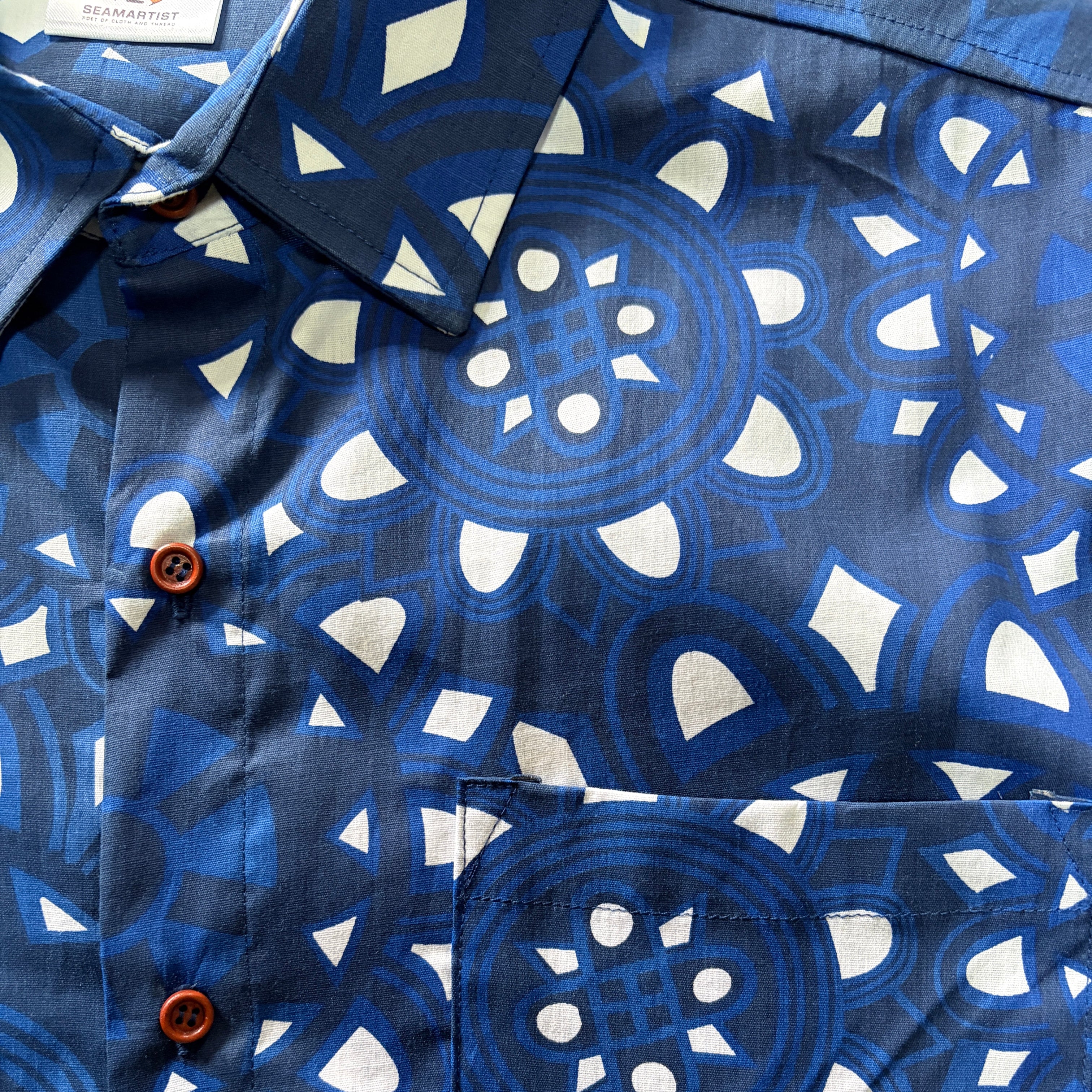 Close-up of a blue and white patterned button-down shirt with brown buttons, showing the collar, front placket, and chest pocket.